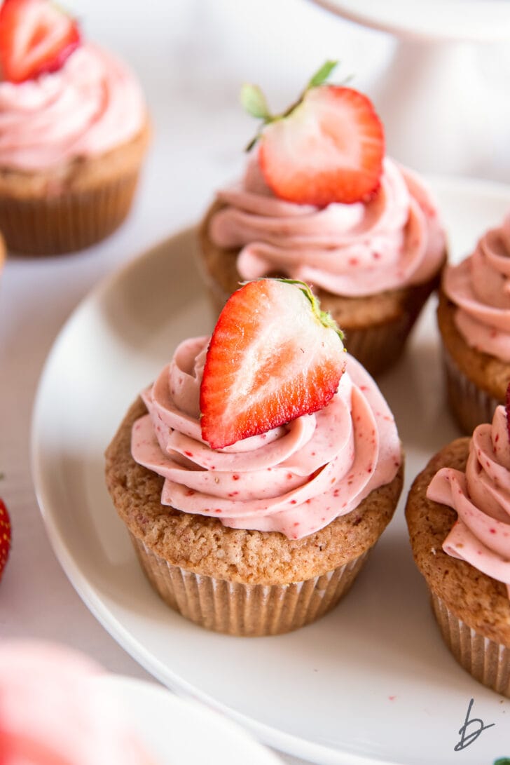 strawberry cupcakes with pink frosting and fresh strawberry garnish on a plate
