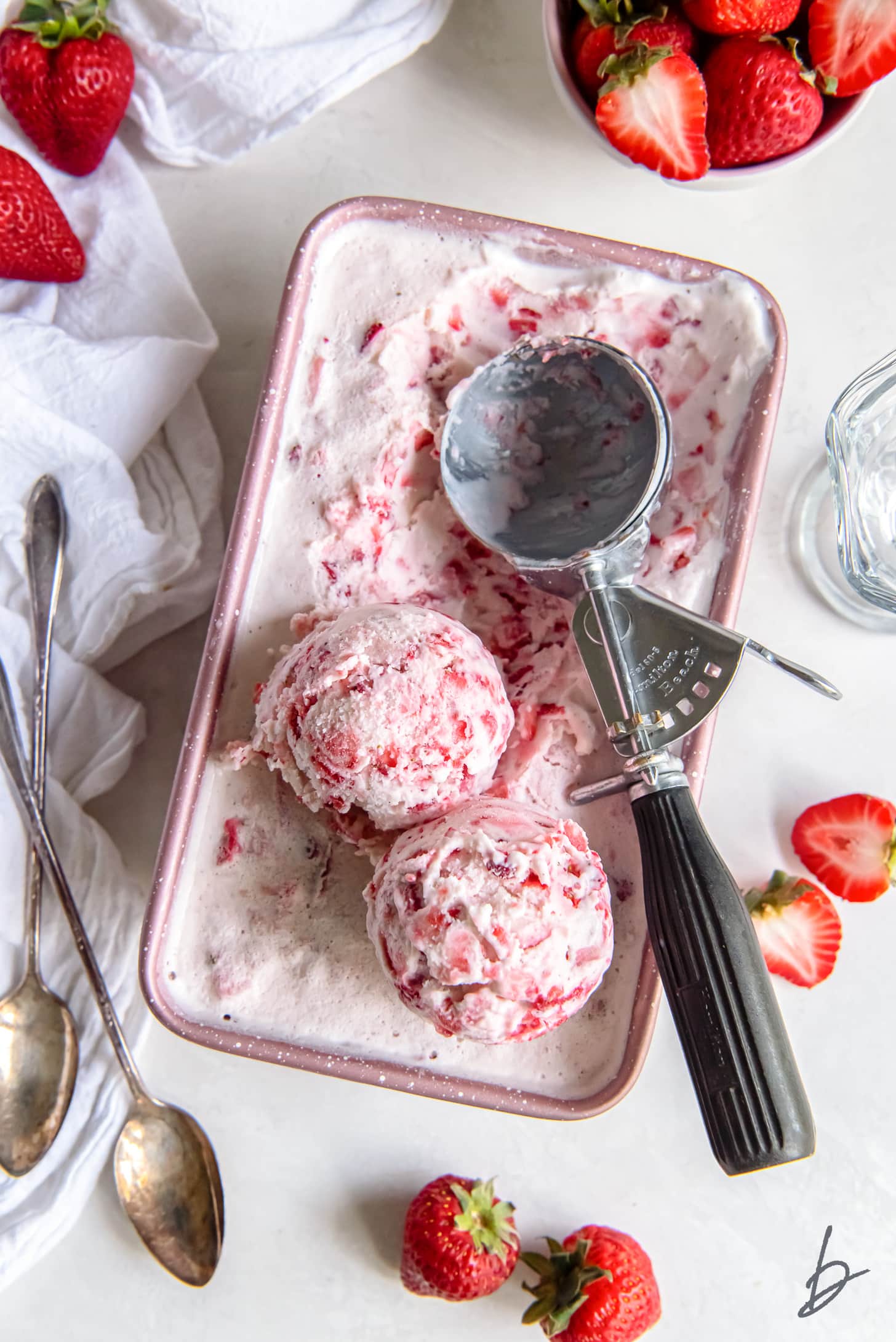 strawberry ice cream in a loaf pan with two scoops sitting on top next to an ice cream scoop