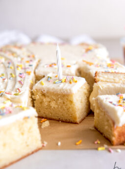 slice of vanilla sheet cake with vanilla frosting sprinkles and white birthday candle