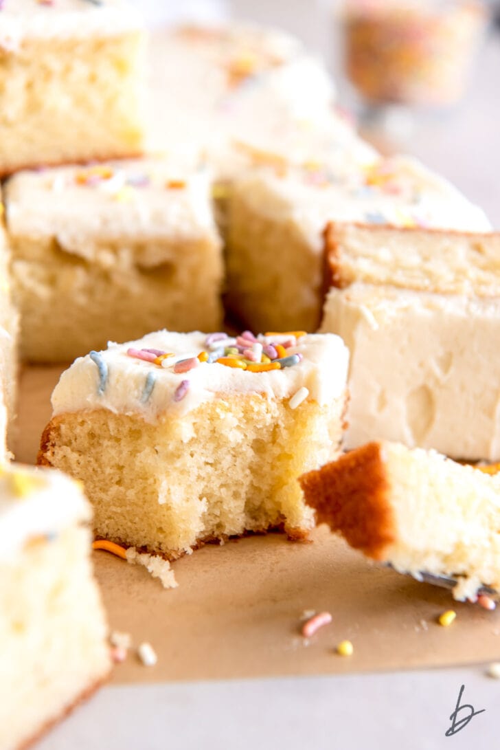 square slice of vanilla sheet cake with vanilla frosting and bite taken from corner of cake slice