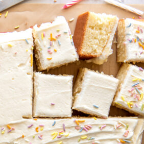 vanilla sheet cake with square slices cut off the corner of the cake