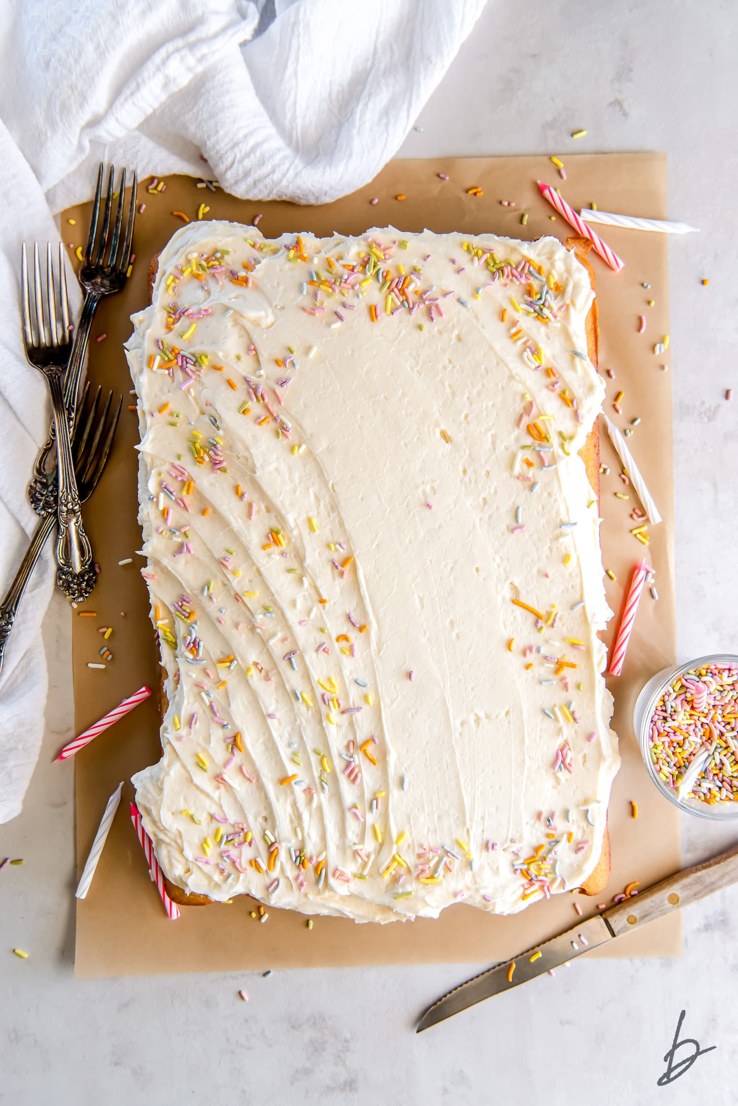 vanilla frosting and sprinkles on rectangle cake on parchment paper