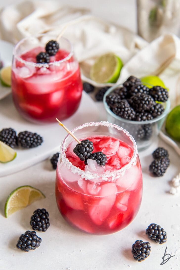 two glasses of blackberry margaritas next to fresh blackberries and lime wedges