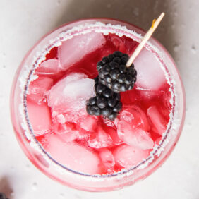 top of a glass filled with blackberry margarita and ice with a skewer of fresh blackberries