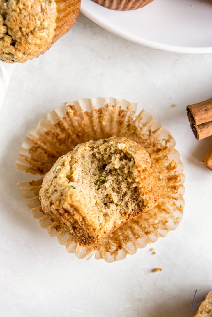 zucchini bread muffins with a bite on an open paper muffin liner