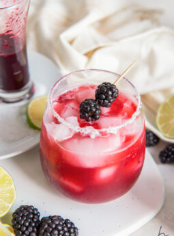 blackberry margarita in a glass with a salted rim and skewer of fresh blackberries