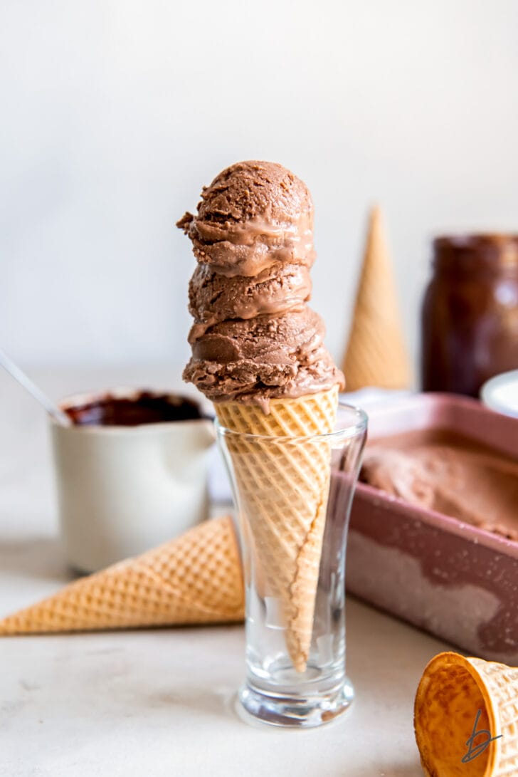 three scoops of chocolate ice cream on a sugar cone in a small glass