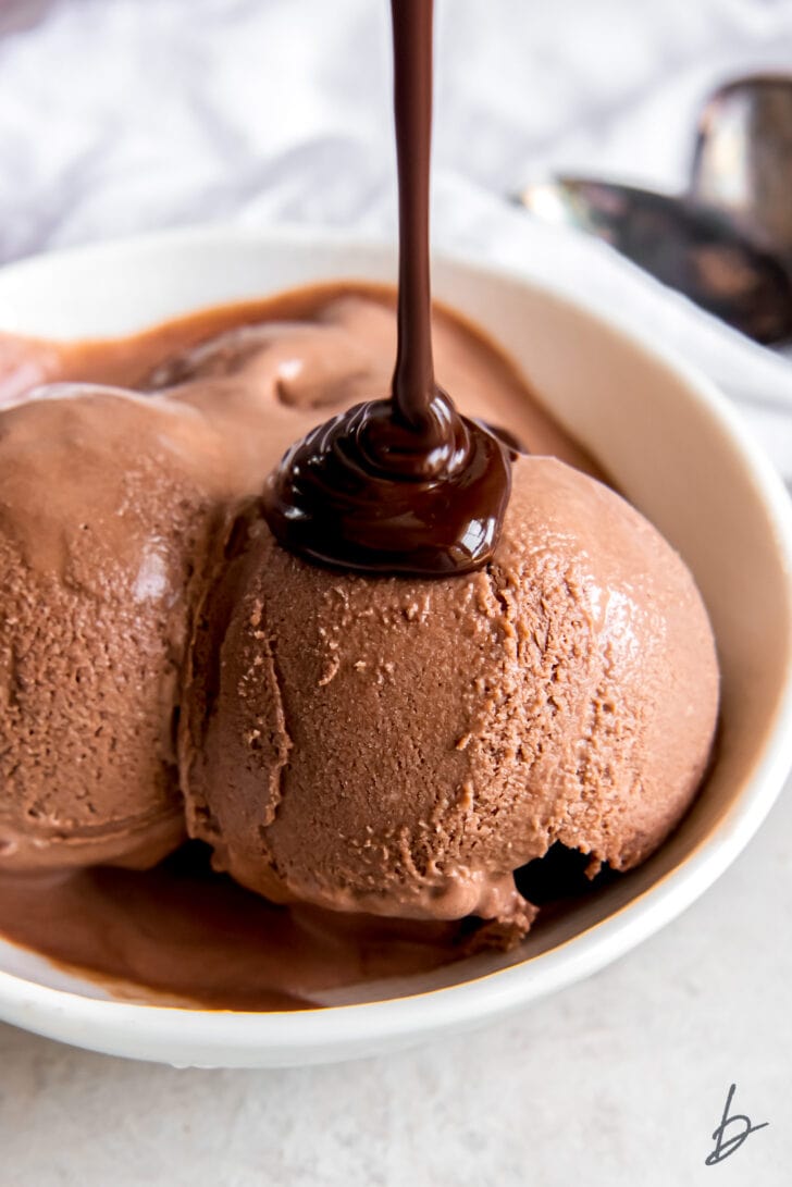 chocolate sauce being poured over scoop of no churn chocolate ice cream in a bowl