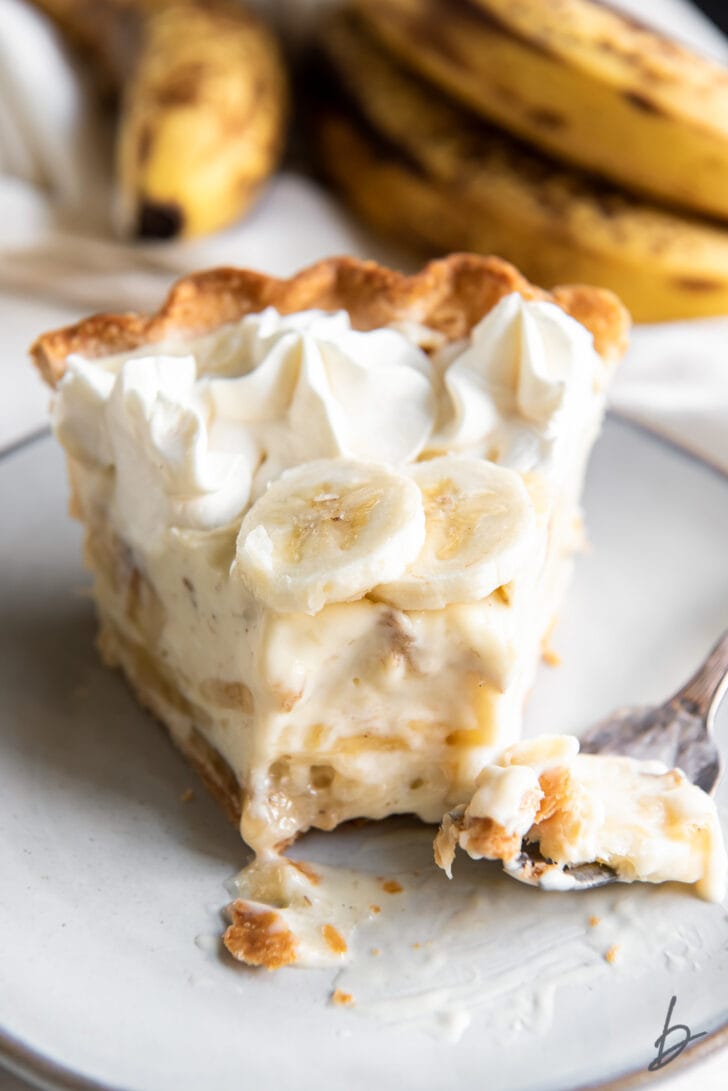 slice of homemade banana cream pie on plate with fork holding a bite