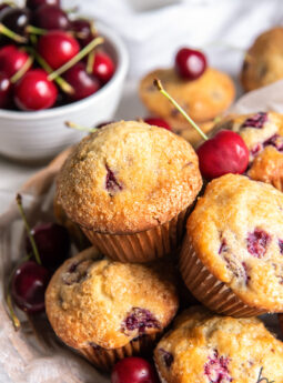 cherry muffins in a pile in front of bowl of fresh cherries