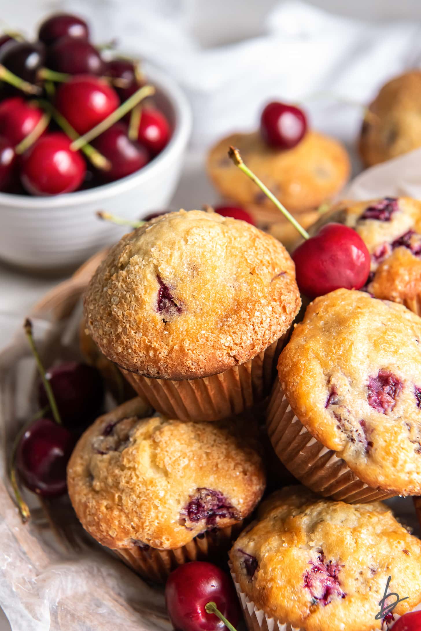 cherry muffins in a pile in front of bowl of fresh cherries