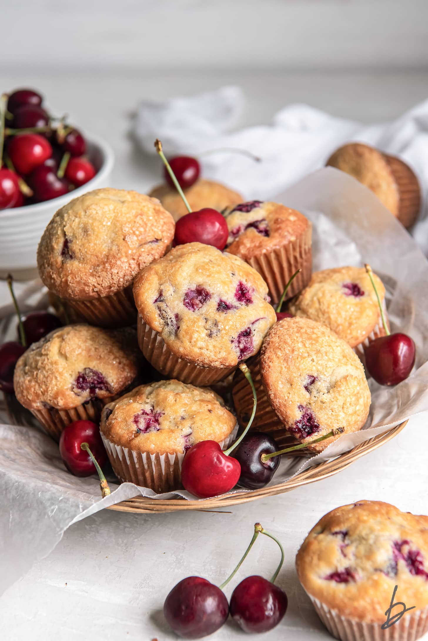 pile of cherry muffins with a few fresh cherries on a shallow basket