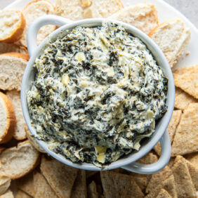 bowl of spinach artichoke dip surrounded by crackers and crostinis