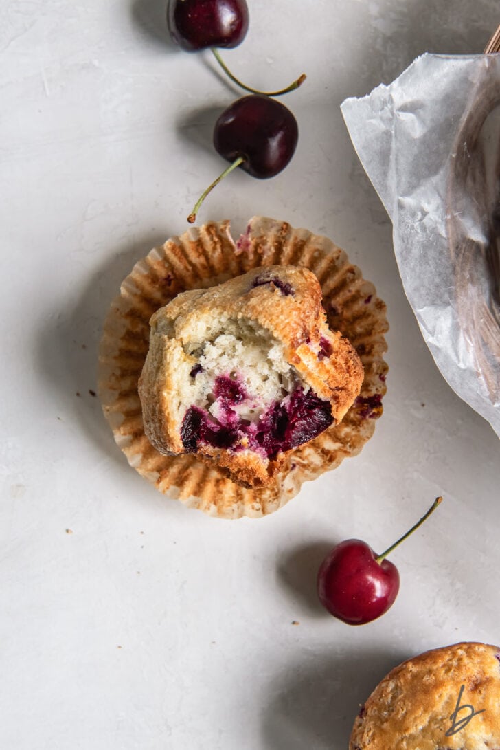 cherry muffin with a bite laying on its side on open paper muffin liner