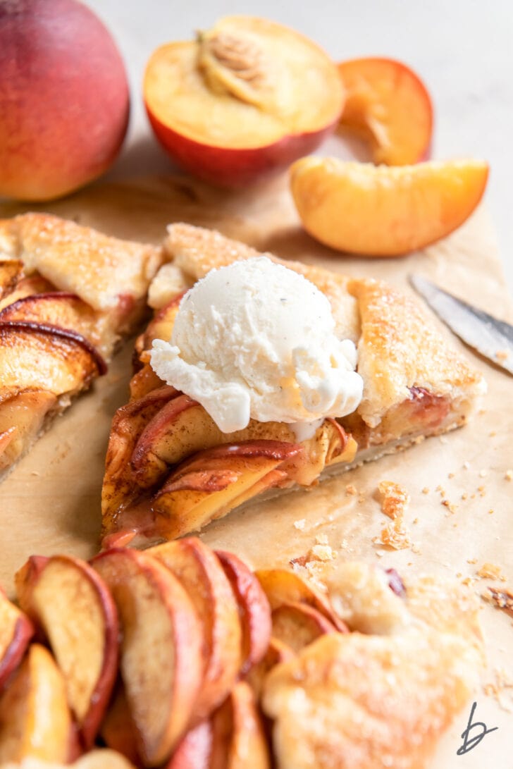 slice of peach galette with an ice cream scoop next to fresh peach slices