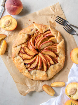 peach galette on parchment paper next to fresh peaches and peach slices
