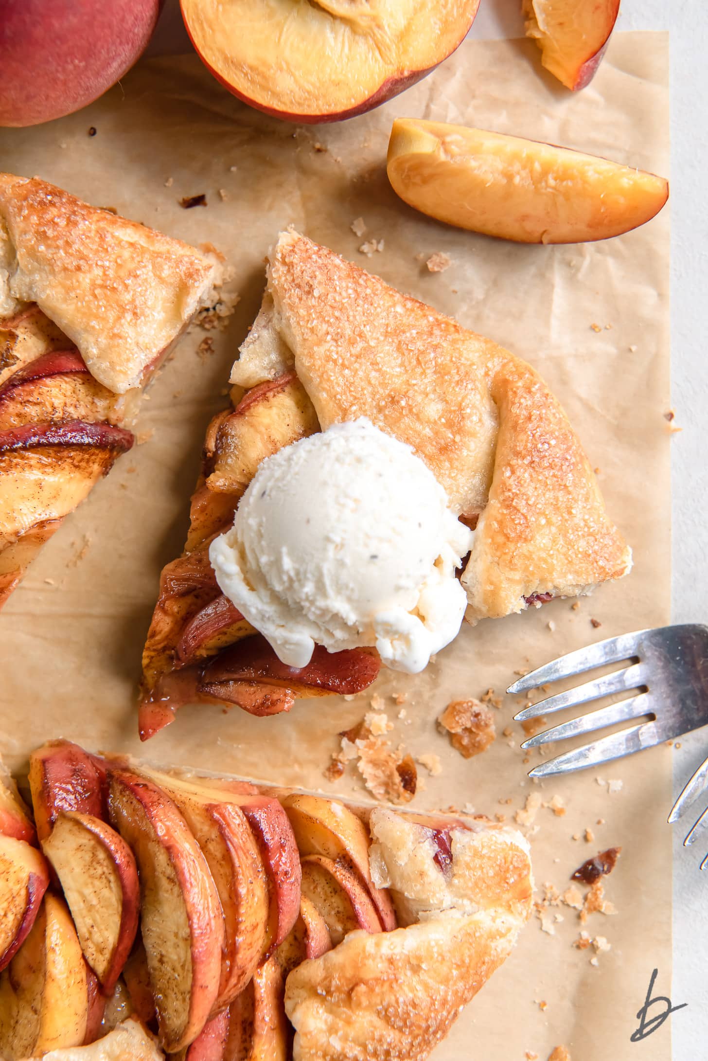 scoop of vanilla ice cream on slice of peach galette on parchment paper next to fork
