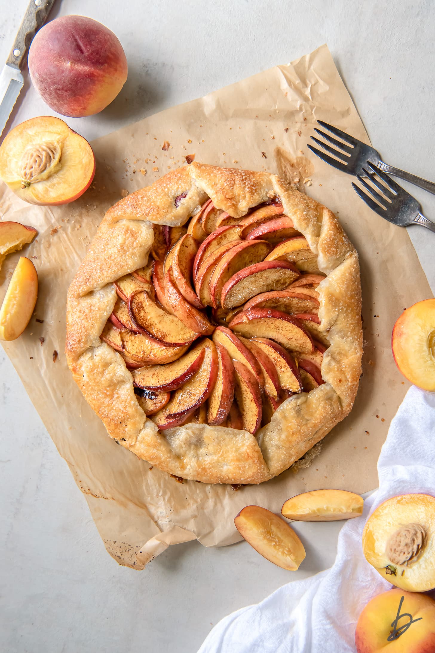 peach galette on parchment paper next to fresh peaches and peach slices