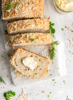 parmesan herb quick bread loaf sliced on marble slab and end slice with pat of butter