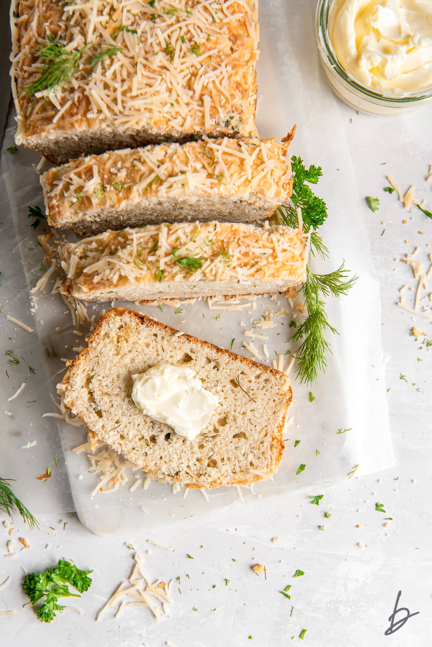 parmesan herb quick bread loaf sliced on marble slab and end slice with pat of butter