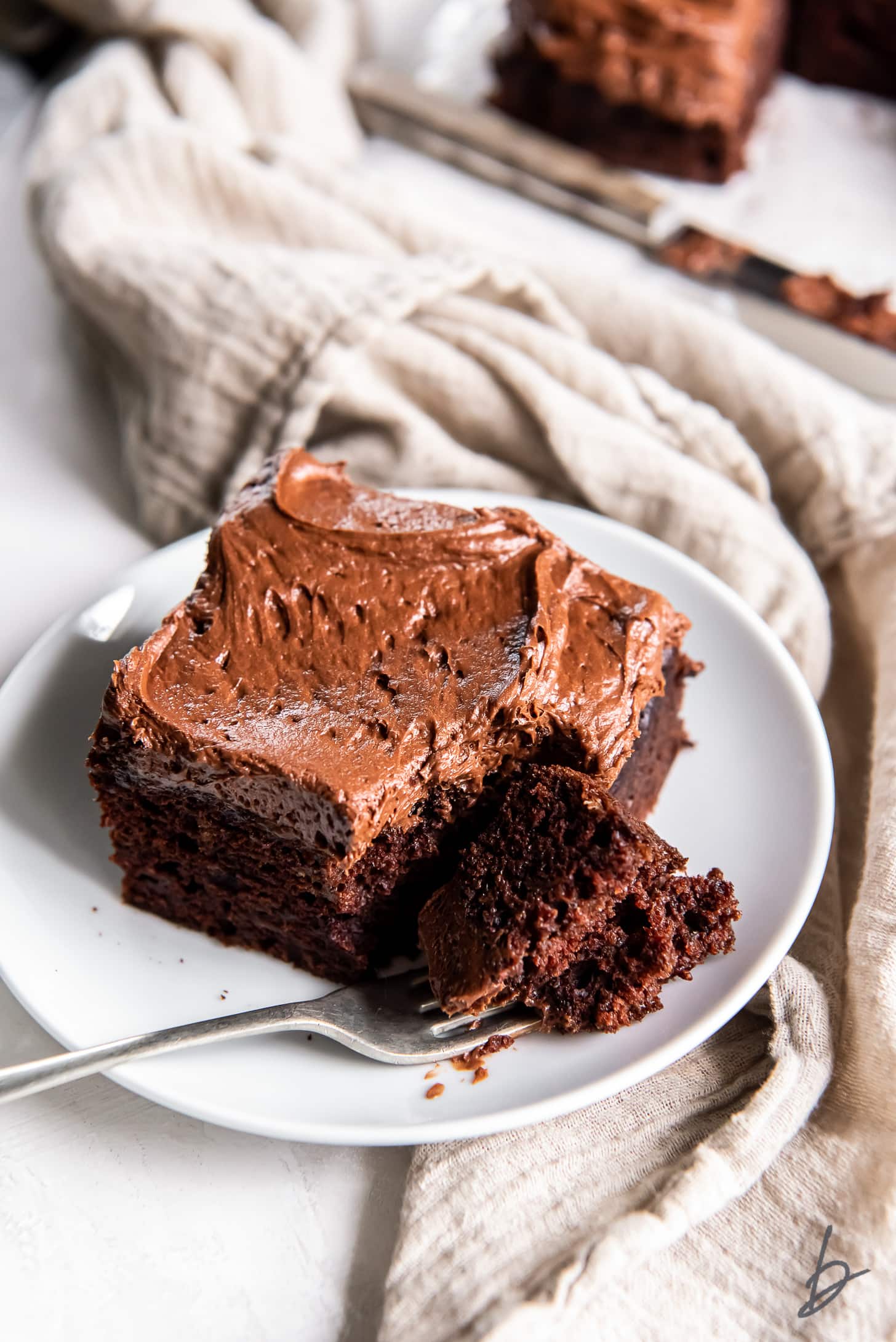 square slice of chocolate zucchini cake on a white plate with fork holding a bite