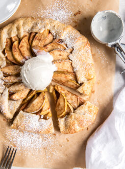 apple galette with scoop of vanilla ice cream on parchment paper next to ice cream scoop.