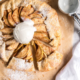 apple galette with scoop of vanilla ice cream on parchment paper next to ice cream scoop.
