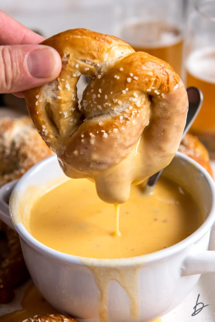 hand holding soft pretzels over bowl of beer cheese dip