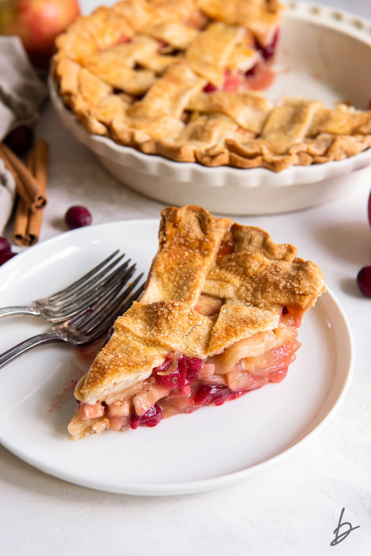 slice of apple cranberry pie on a white plate with two forks.