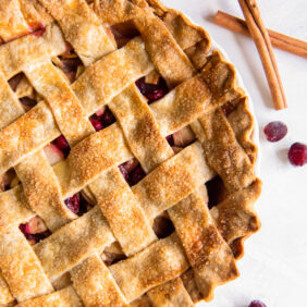 cranberry apple pie with lattice crust next to cinnamon sticks and fresh cranberries.