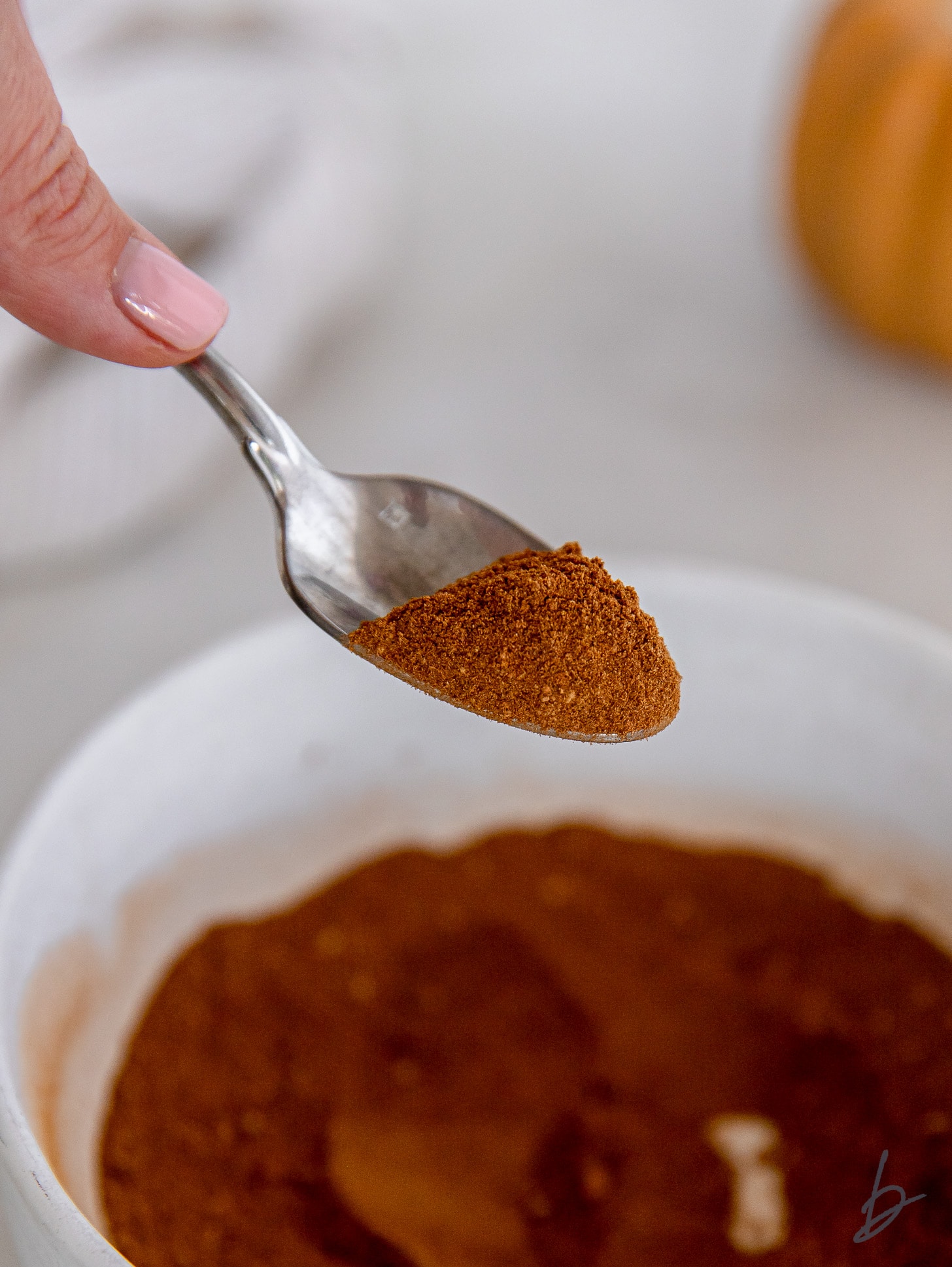 spoon holding pumpkin pie spice over bowl with more spice blend