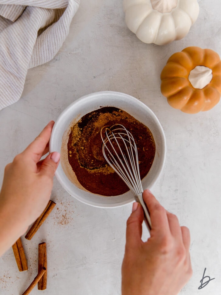 hand holding whisk combining pumpkin pie spices in a bowl