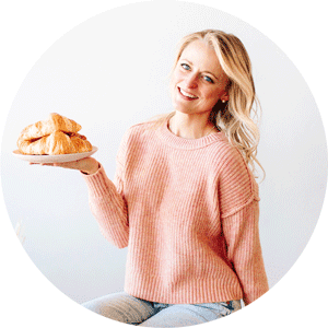 blonde woman in pink sweater holding plate of croissants