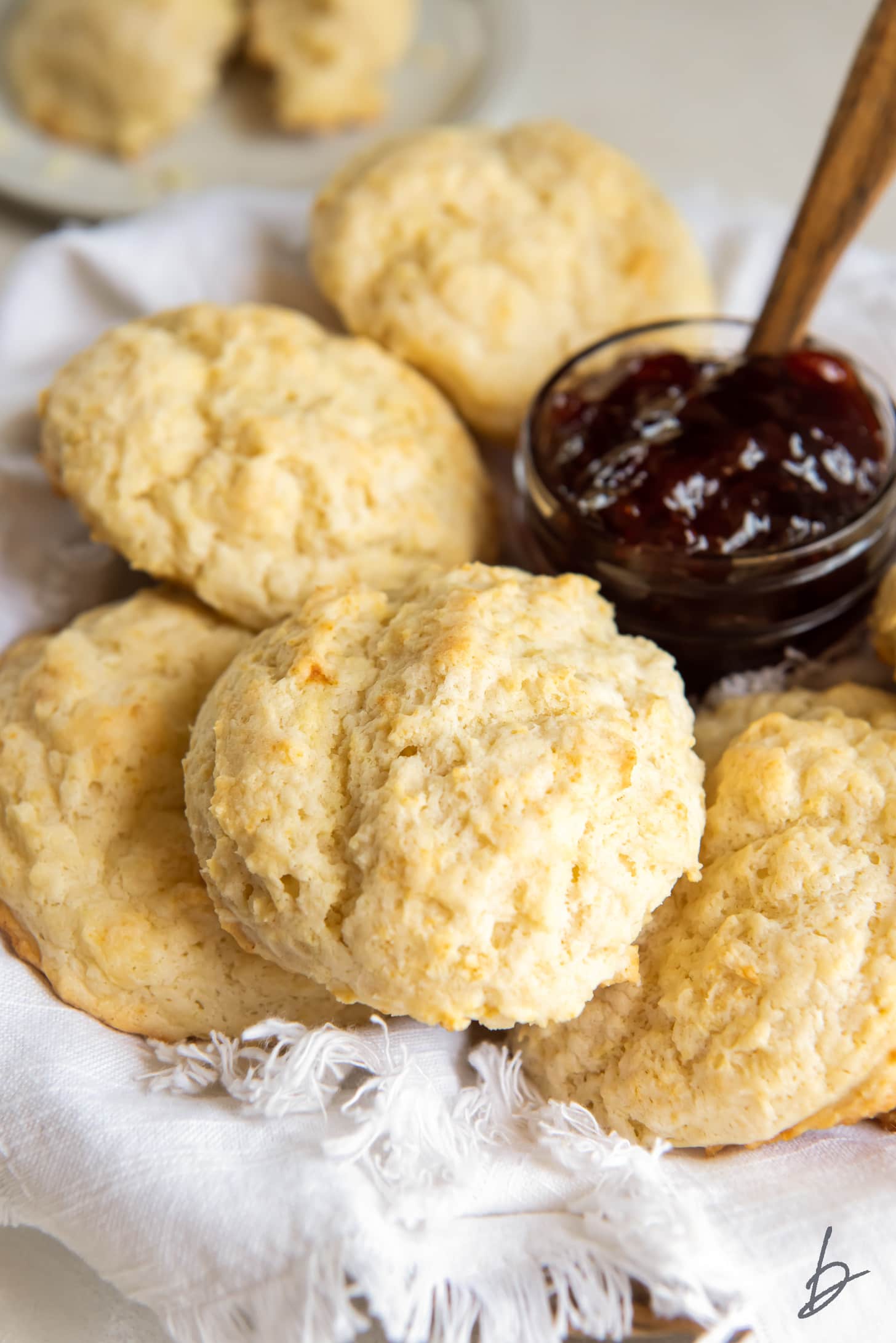 buttermilk drop biscuits on cloth in basket next to jar of jam.