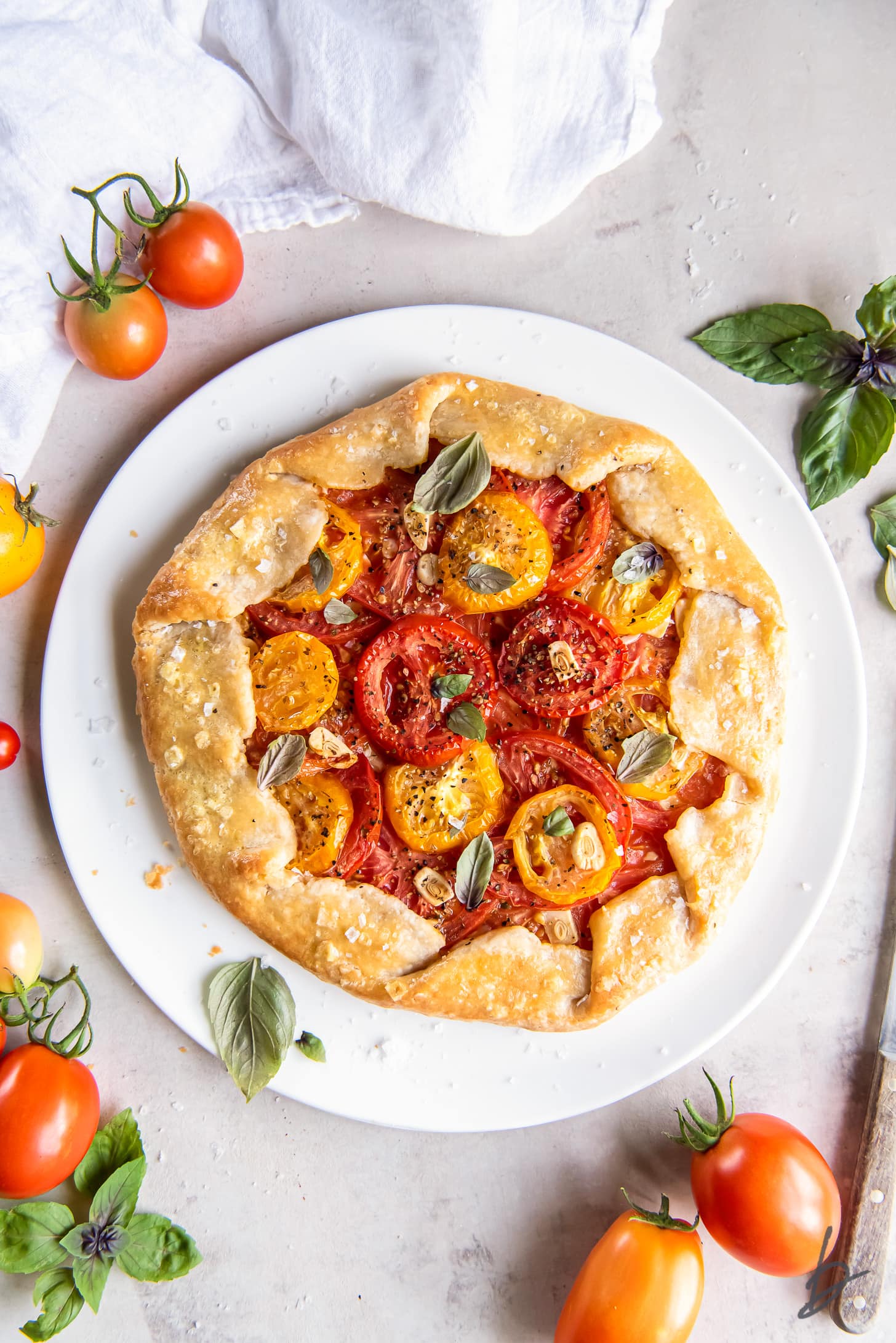 tomato galette on large white plate next to fresh tomatoes and basil