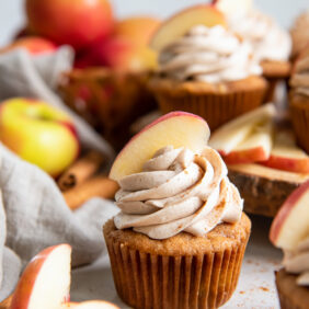 apple spice cupcake with frosting and apple slice garnish next to more apple slices.