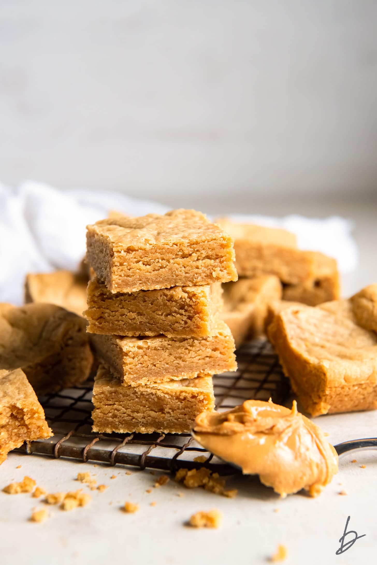 stack of peanut butter cookie bars next to more bars and spoonful of peanut butter.