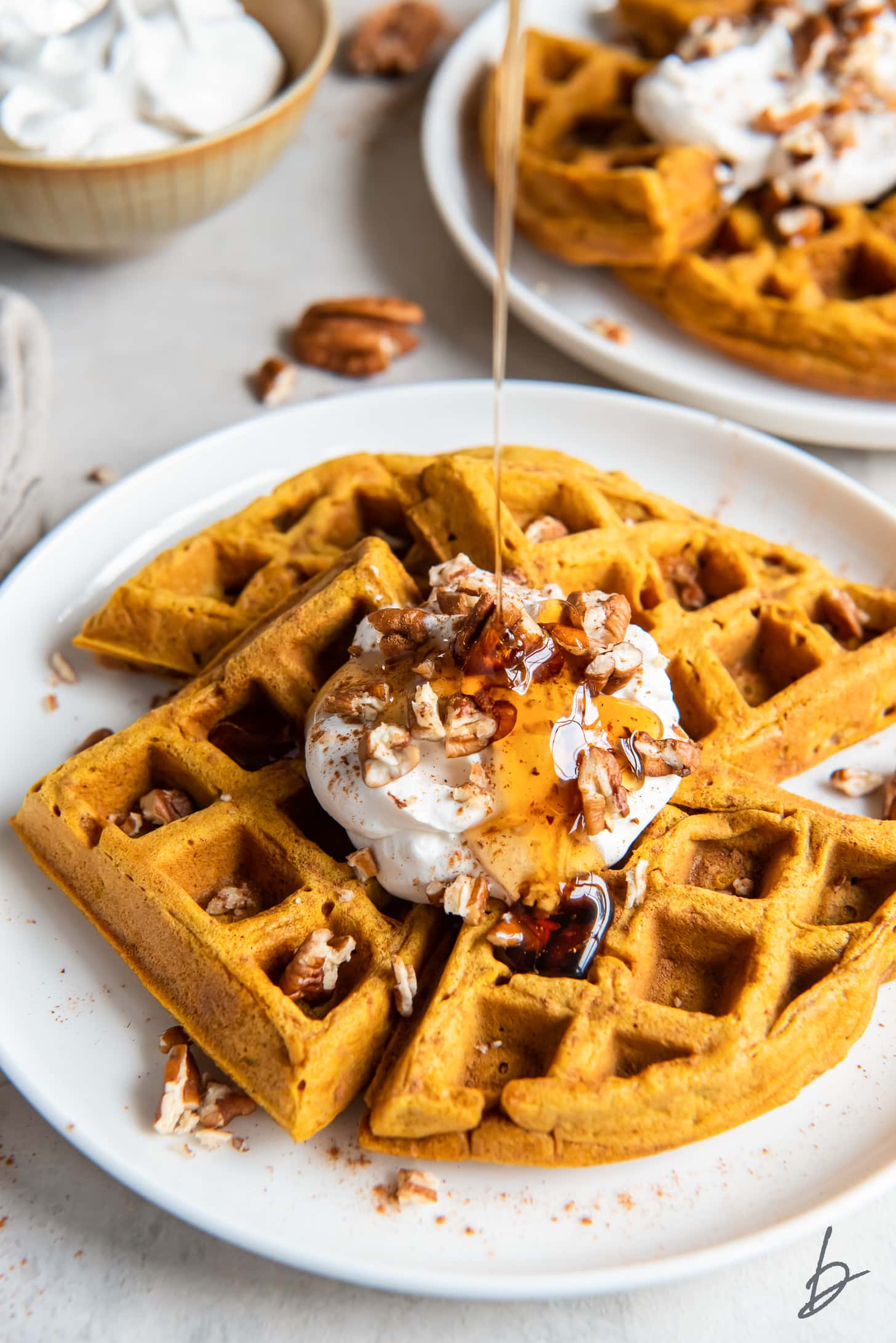 pumpkin waffles topped with whipped cream, chopped pecans and drizzle of maple syrup.
