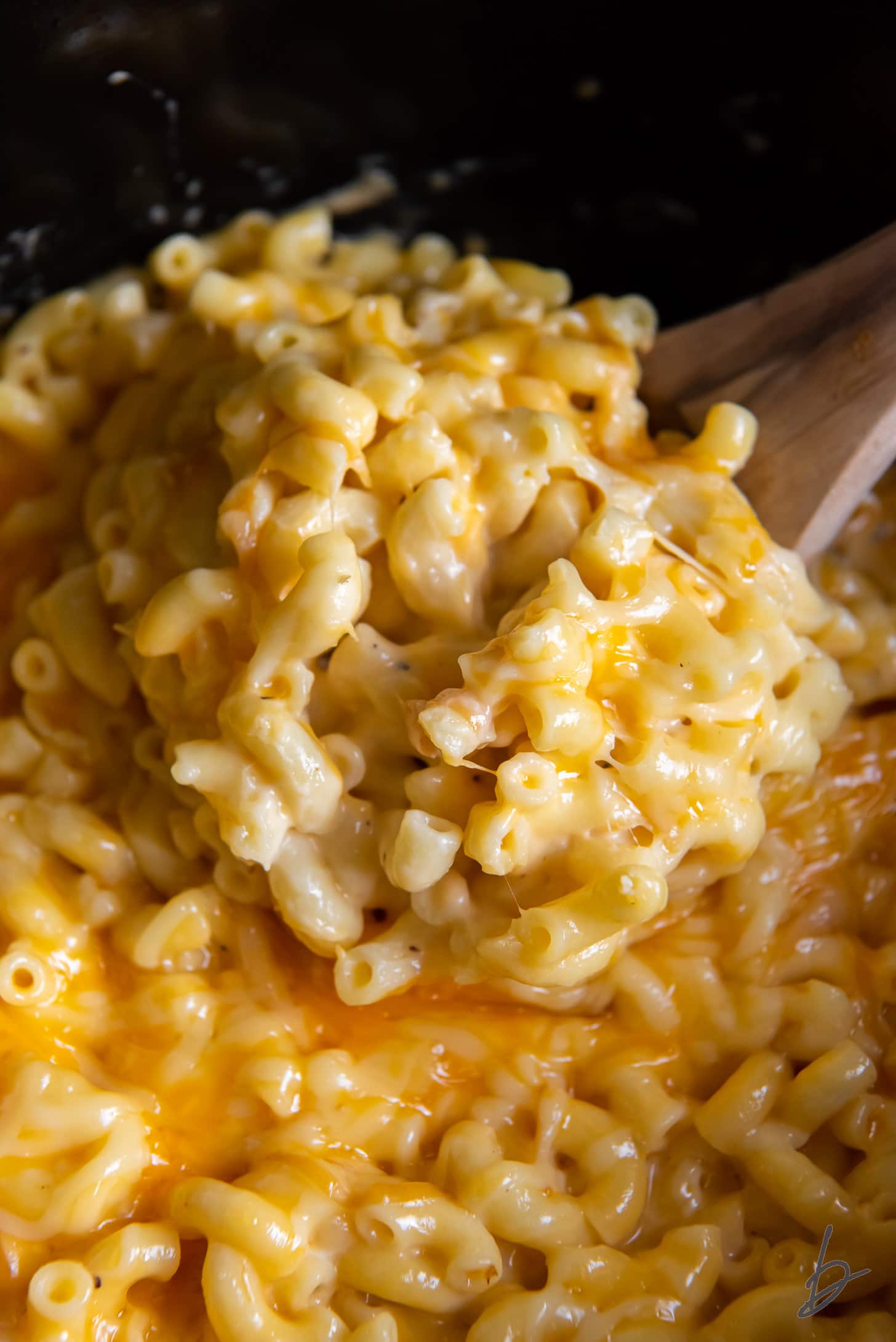 wooden spoon stirring creamy mac and cheese in a crockpot.