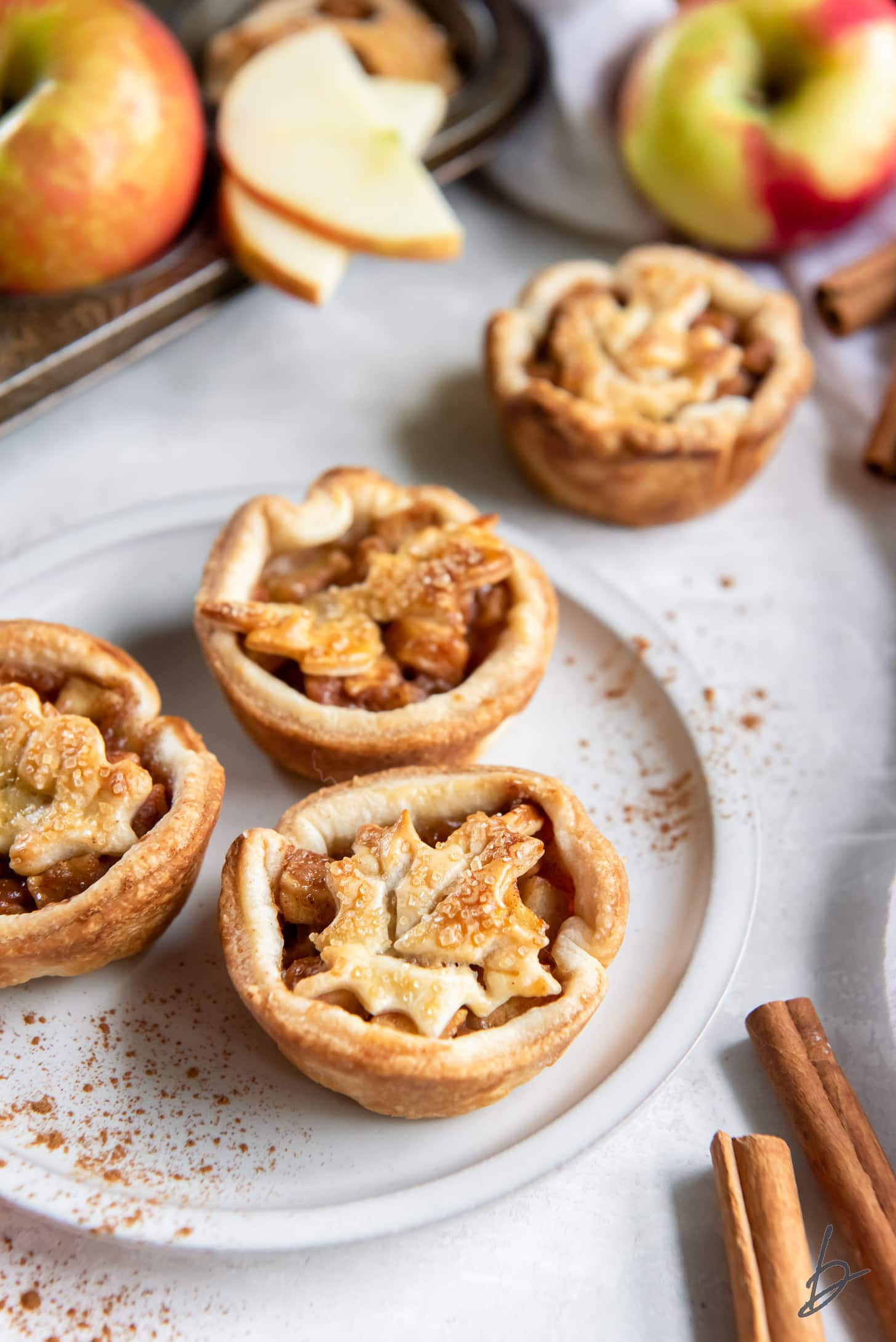 plate with three individual apple pies next to cinnamon sticks.