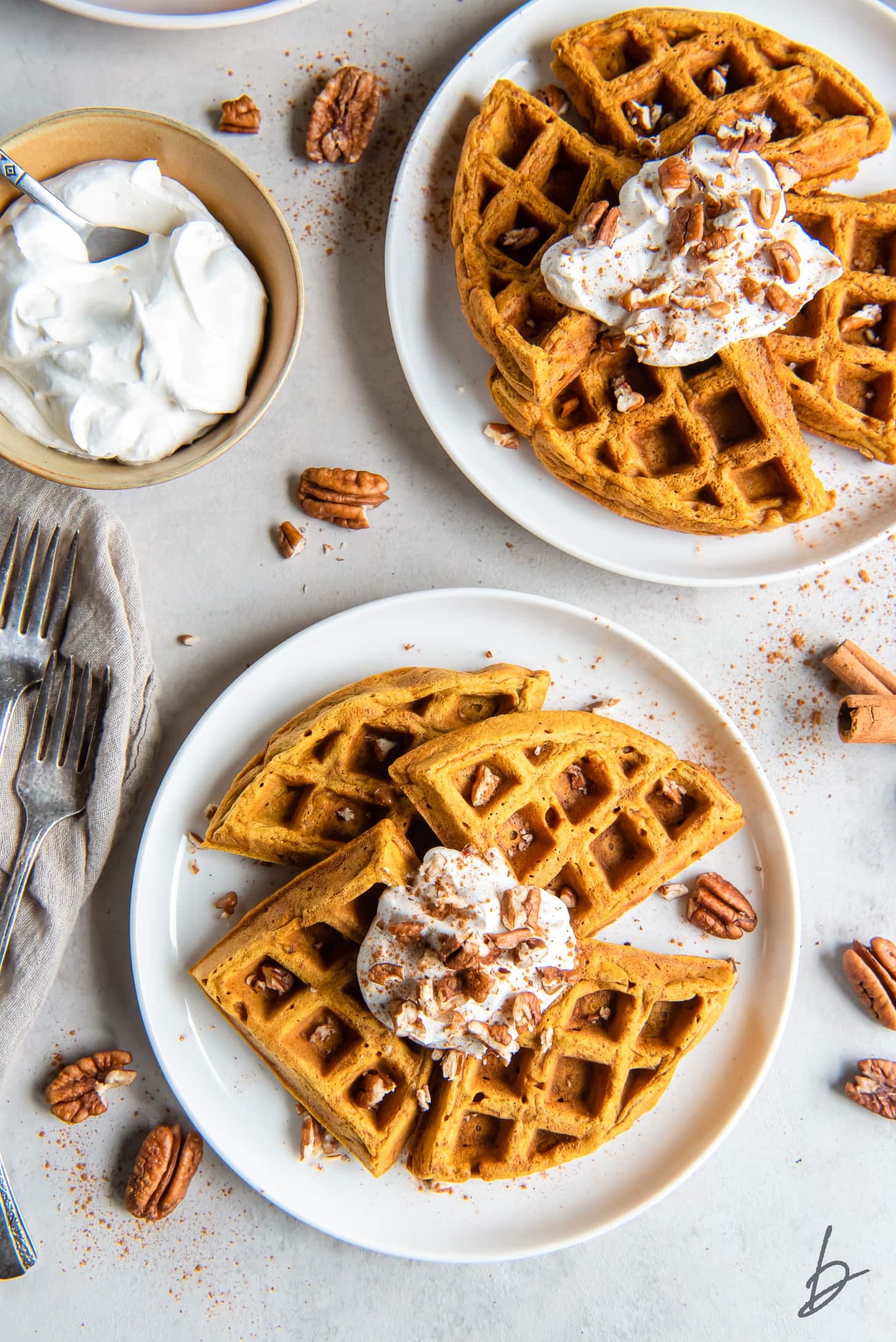 two plates of pumpkin waffles with whipped cream and pecan topping.