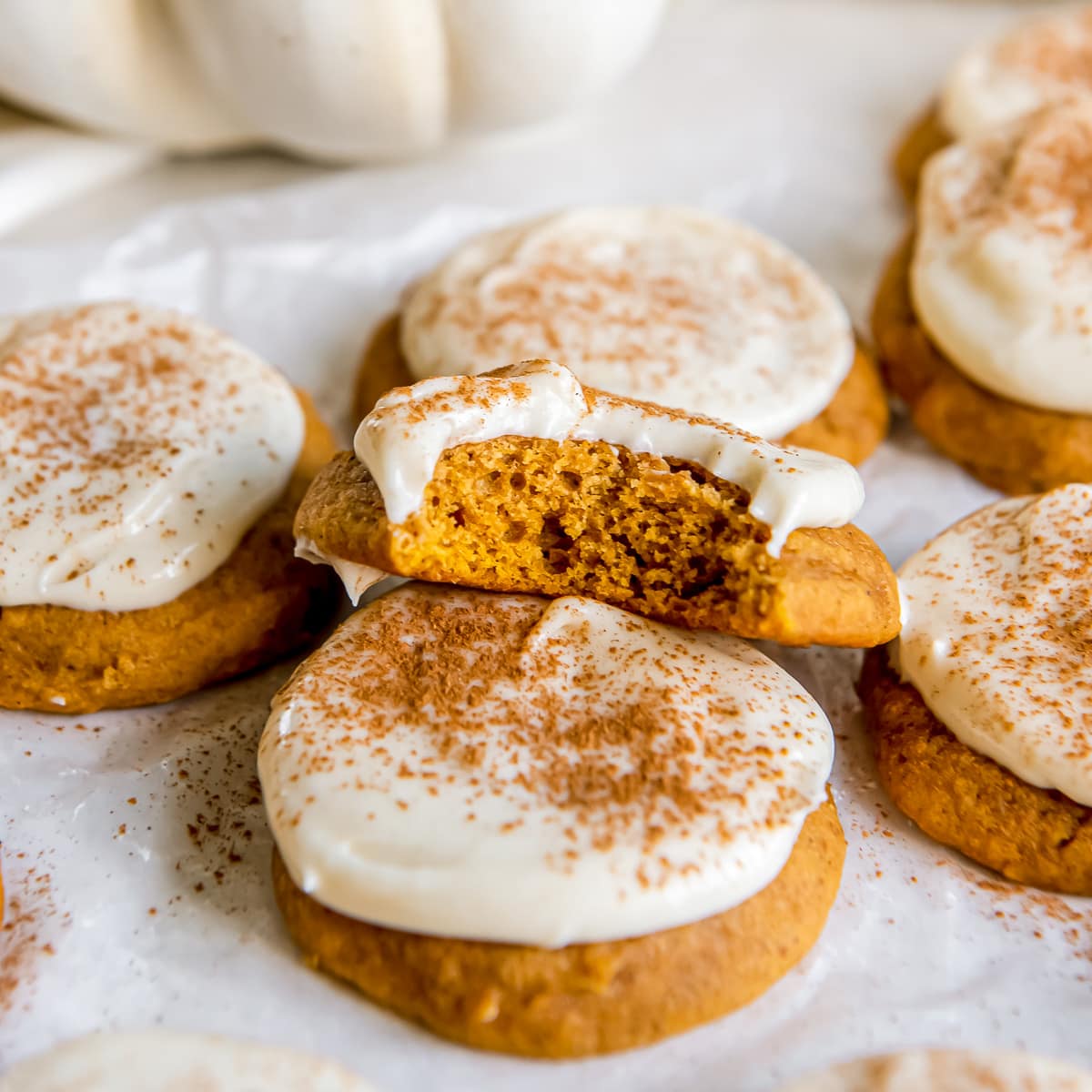 frosted pumpkin cookie with a bite propped on another cookie.