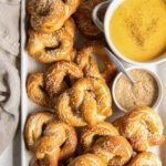 soft pretzels on baking sheet with bowl of beer cheese dip and bowl of mustard.