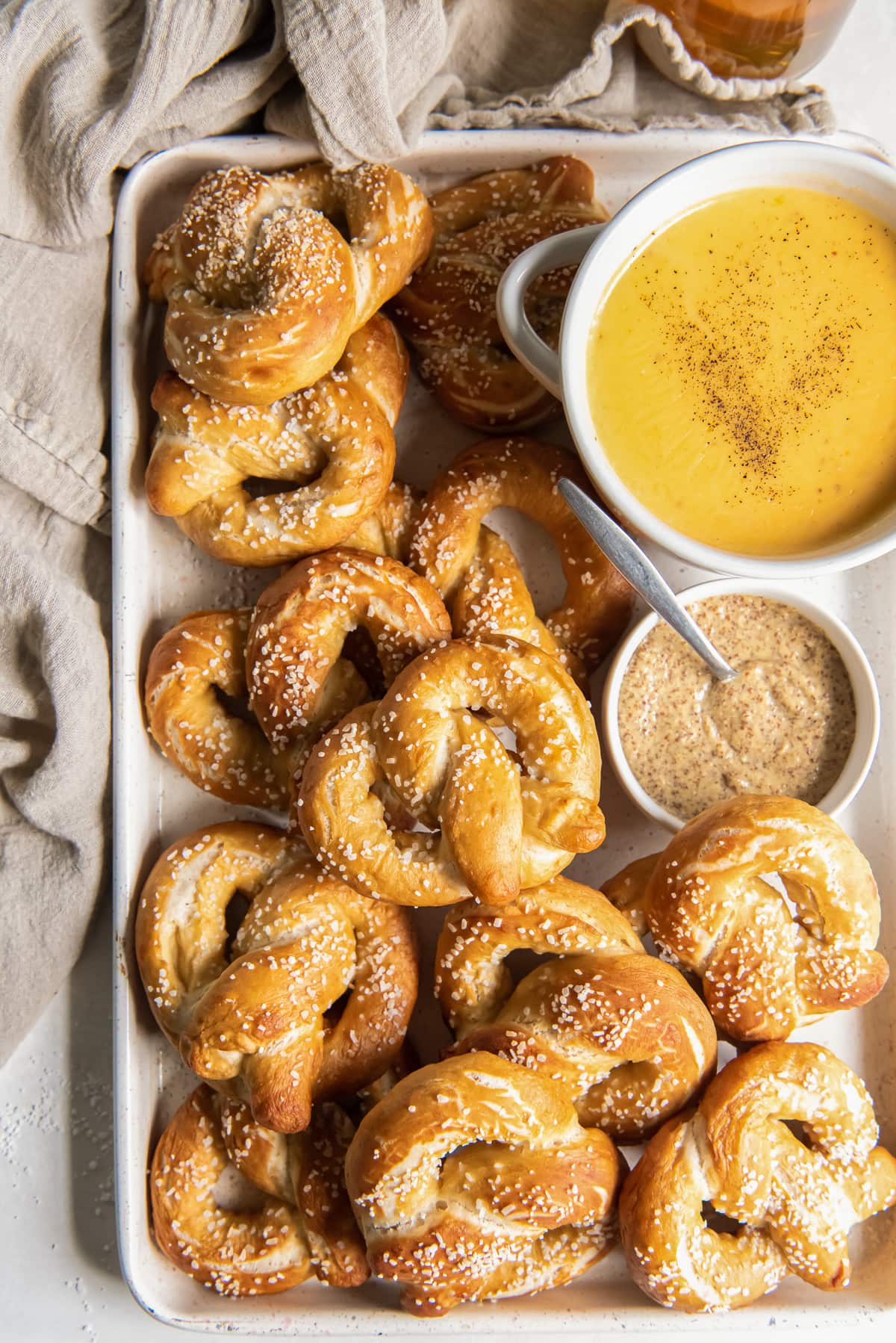 soft pretzels on baking sheet with bowl of beer cheese dip and bowl of mustard.