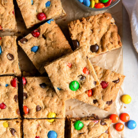 square monster cookie bar on top of more bars with m&ms.