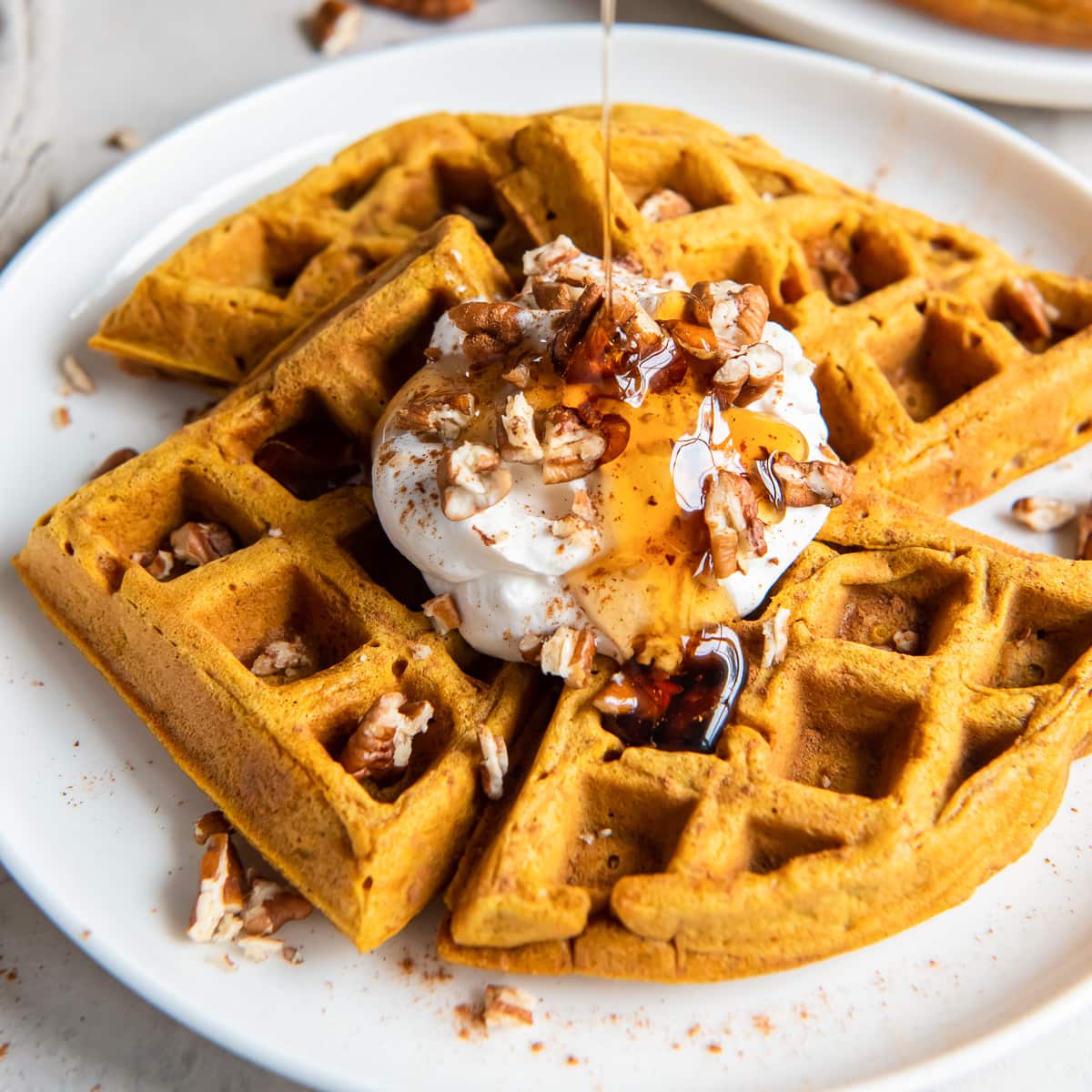 plate of pumpkin waffles with whipped cream, pecans and syrup.