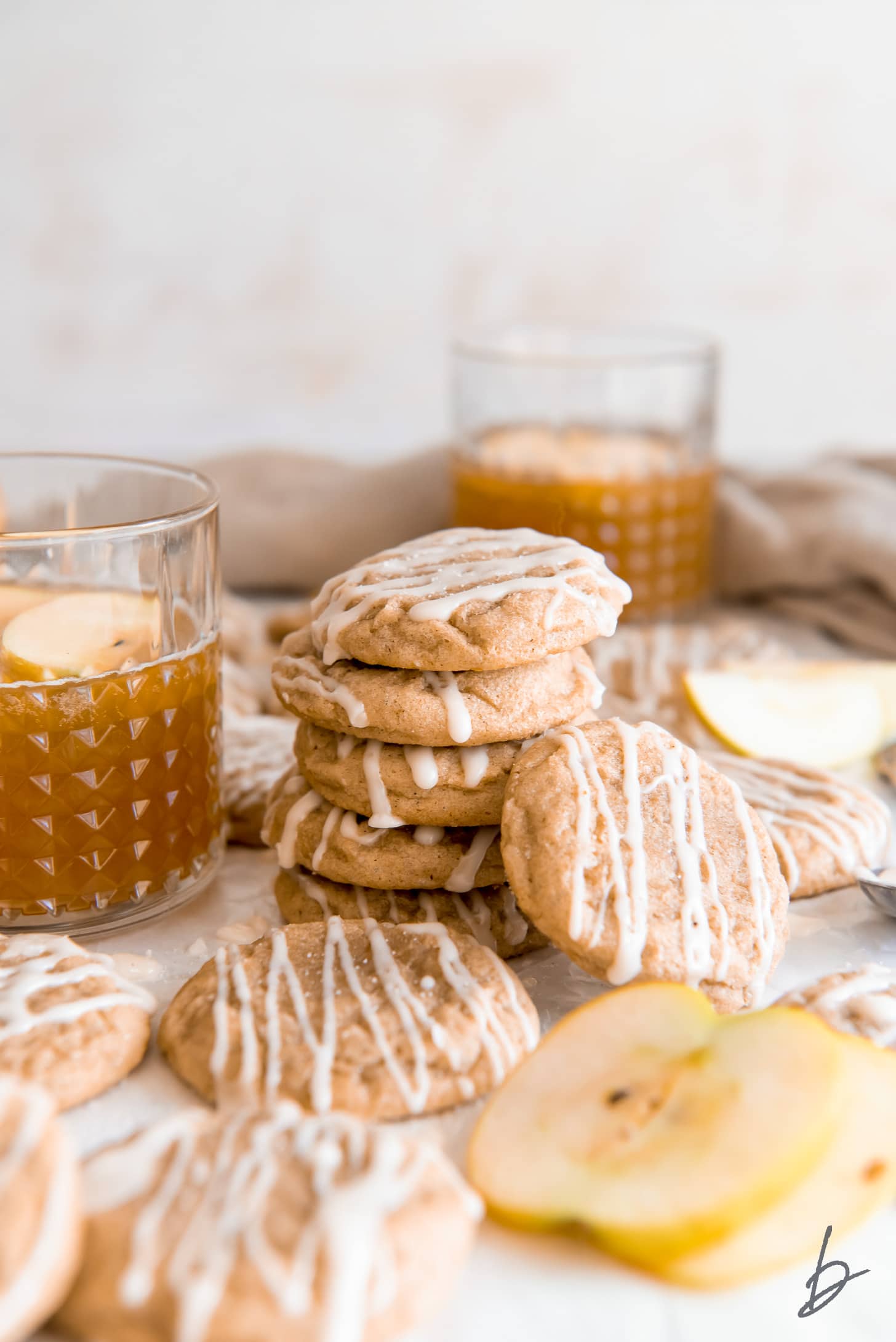 apple cider cookie leaning against stack of cookies in front of glass of apple cider.