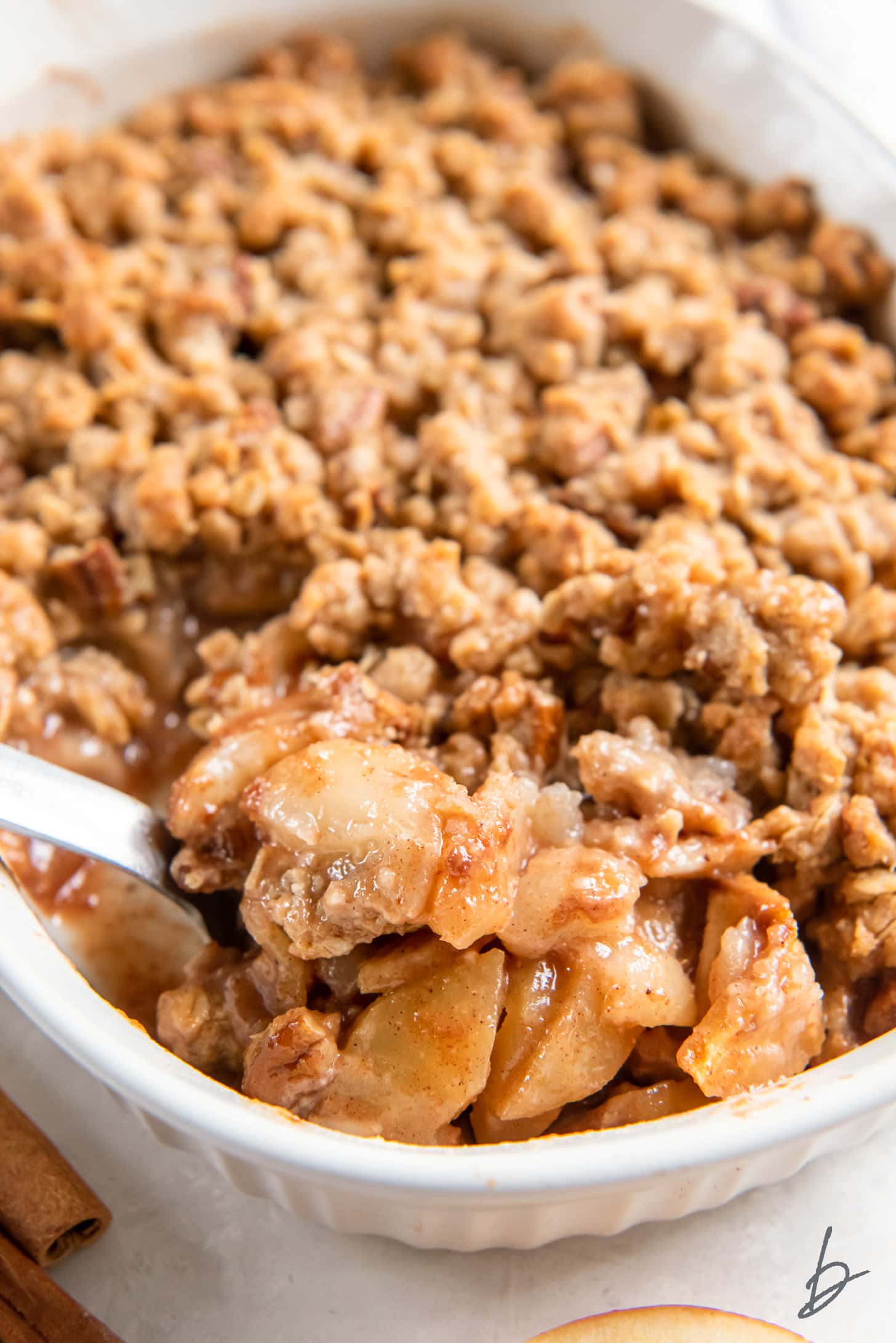 serving spoon lifting scoop of apple pear crisp from a baking dish.