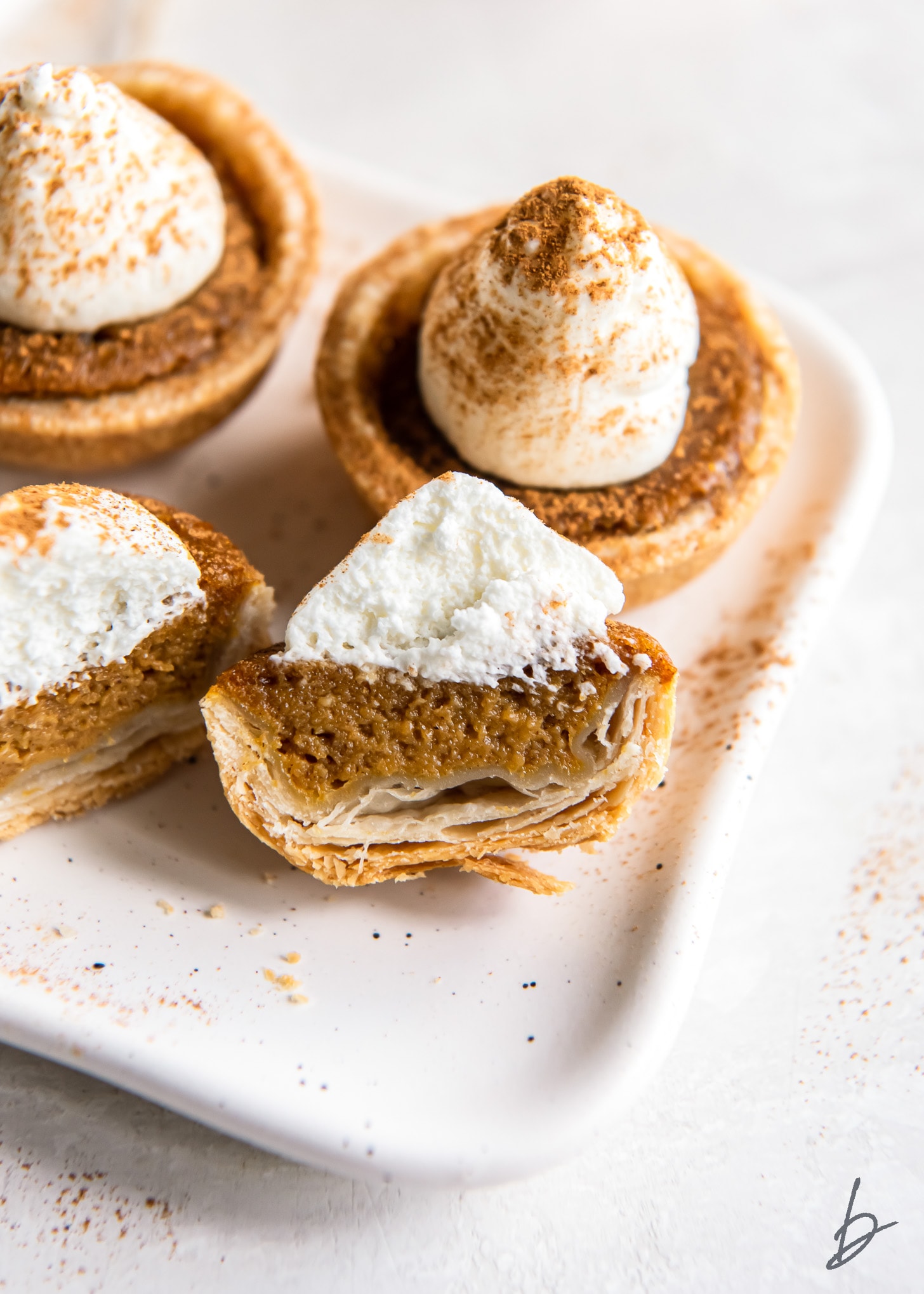 mini pumpkin pie with whipped cream cut in half to show filling and flaky crust.