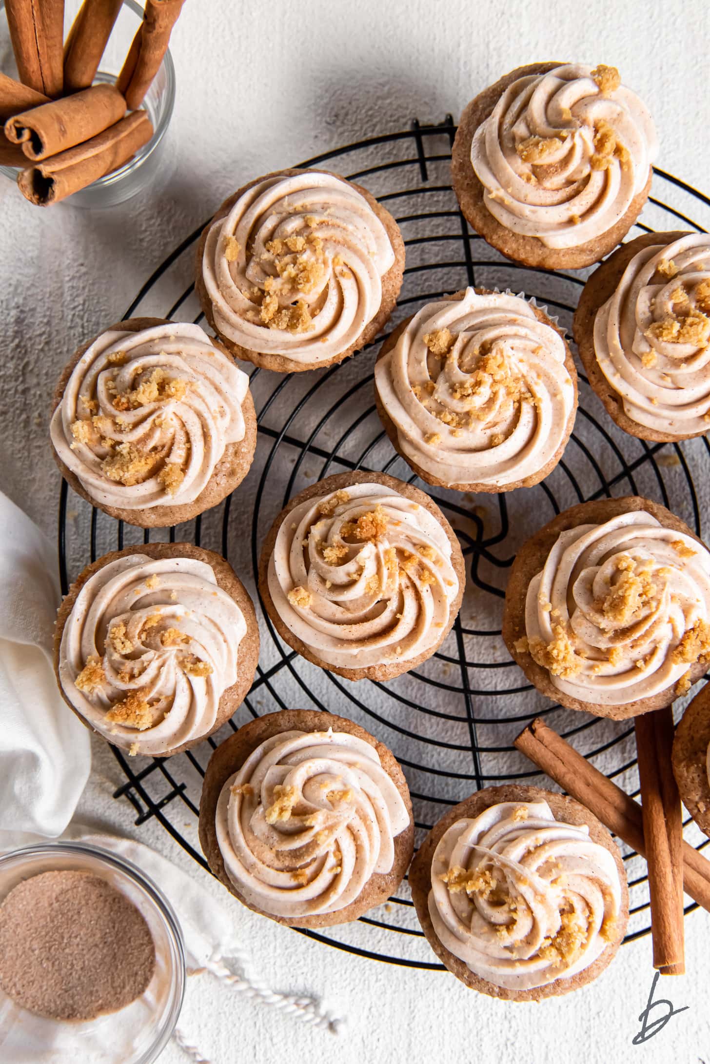 snickerdoodle cupcakes with cinnamon cream cheese frosting on round wire rack.